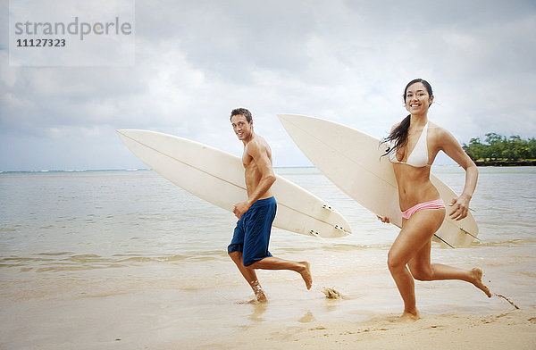 Paar läuft am Strand mit Surfbrettern