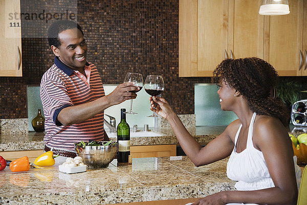 Afrikanisches Paar stößt in der Küche mit Rotwein an