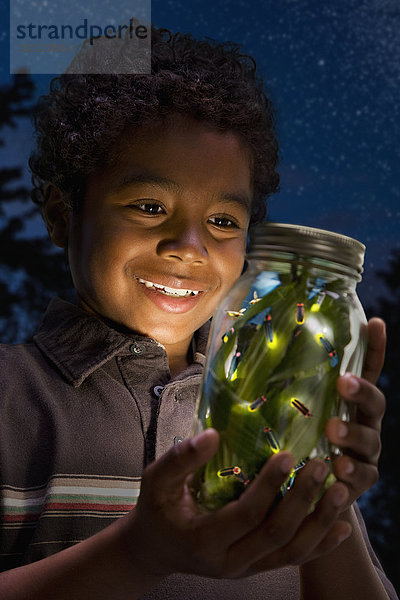 Afrikanischer Junge betrachtet Glühwürmchen im Glas