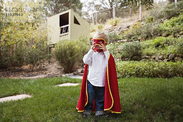 Junge mit Umhang und Maske im Hinterhof