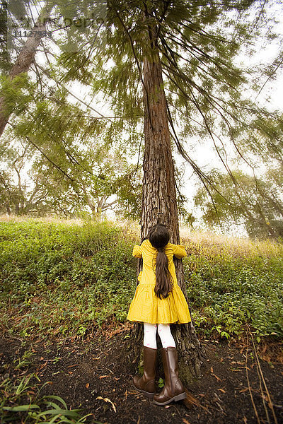 Gemischtrassiges Mädchen  das einen Baum umarmt
