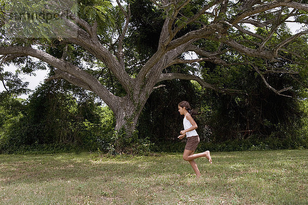 Hispanisches Mädchen läuft barfuß durch Gras