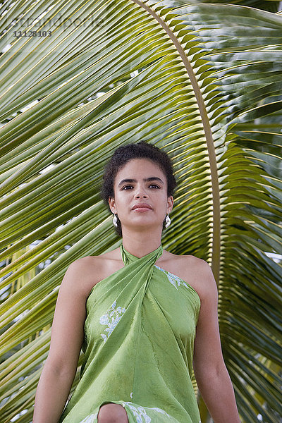 Hispanische Frau im Sarong in der Nähe von Palmblättern