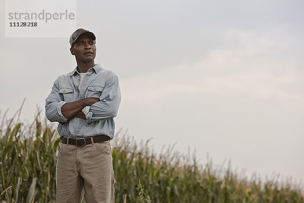 Afroamerikanischer Mann steht mit verschränkten Armen auf einem Feld