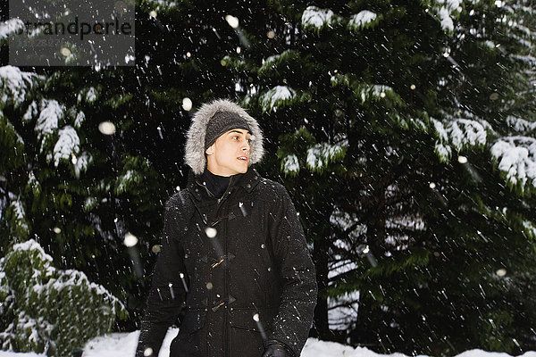 Gemischtrassiger Mann in Kapuzenmantel im Freien bei Schneefall
