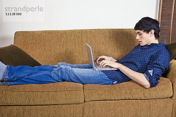 Gemischtrassiger Mann tippt auf einem Laptop auf dem Sofa