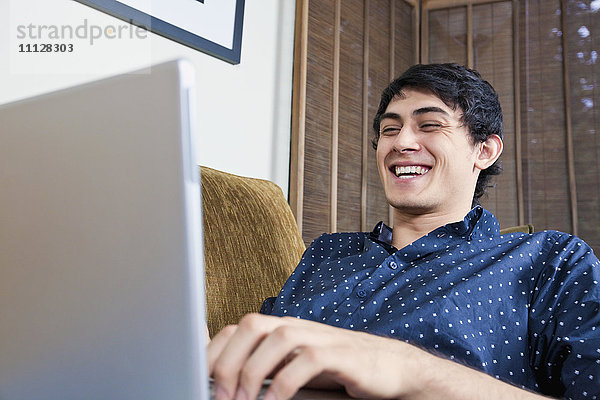 Lachender Mann gemischter Rasse  der auf einem Laptop tippt