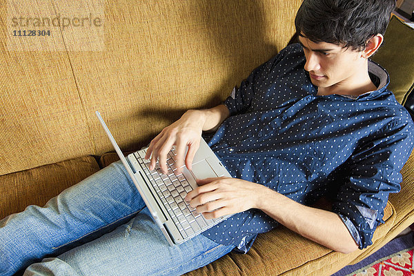 Gemischtrassiger Mann tippt auf einem Laptop auf dem Sofa