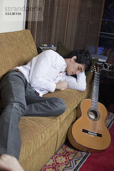 Gemischtrassiger Mann schläft auf dem Sofa neben der Gitarre