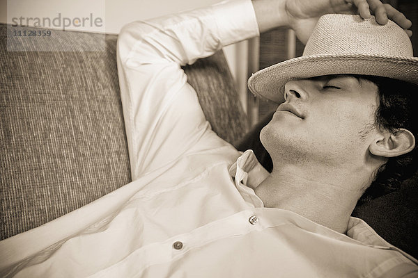Gemischtrassiger Mann schläft auf Sofa mit Hut über dem Gesicht