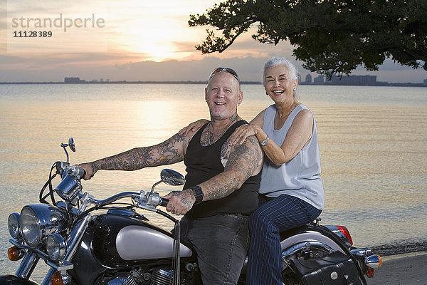 Mutter und tätowierter Sohn fahren Motorrad am Strand