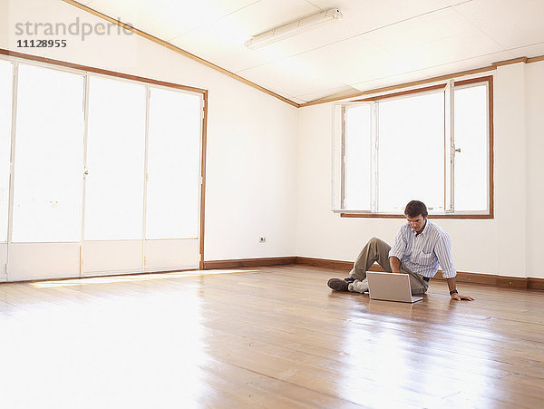Hispanischer Geschäftsmann mit Laptop auf dem Boden in einem leeren Büro