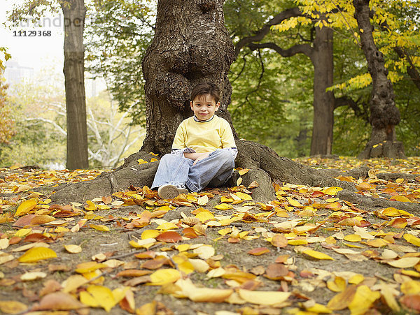 Hispanischer Junge sitzt in der Nähe eines Baumes im Herbst