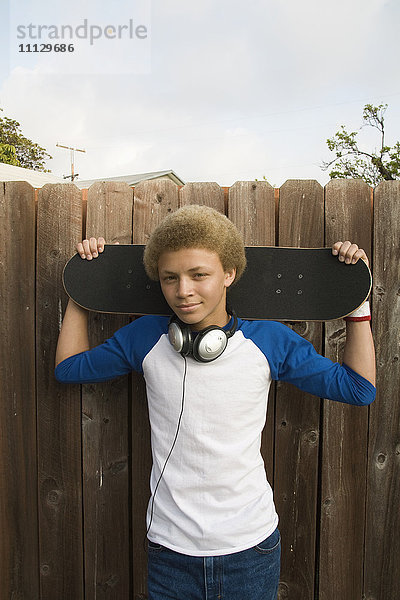 Gemischtrassiger Junge mit Kopfhörern und Skateboard