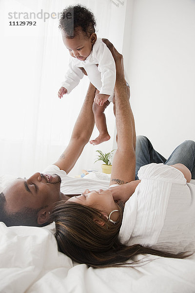 Afrikanisches Paar hält Baby im Bett hoch