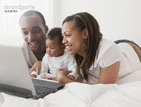 Afrikanisches Paar und Baby mit Laptop auf dem Bett