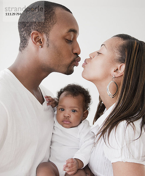 Afrikanisches Paar hält Baby und küsst sich