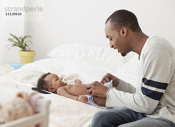Afrikanischer Mann wechselt die Windel eines Babys im Bett