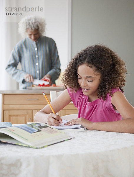 Mädchen macht Hausaufgaben mit Großmutter im Hintergrund