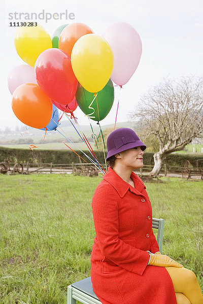 Gemischtrassige Frau hält bunten Strauß Luftballons