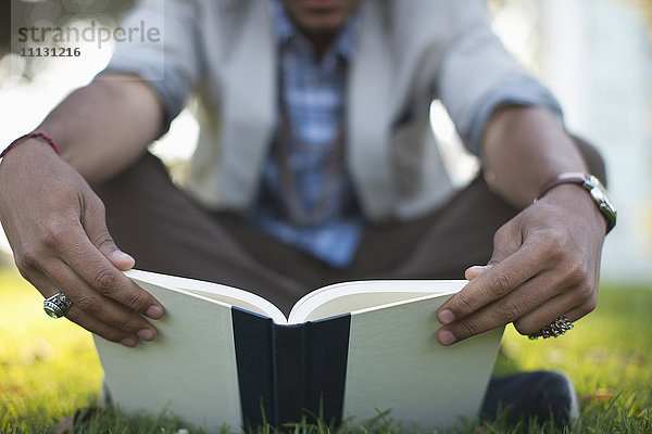 Hispanischer Mann liest Buch im Gras