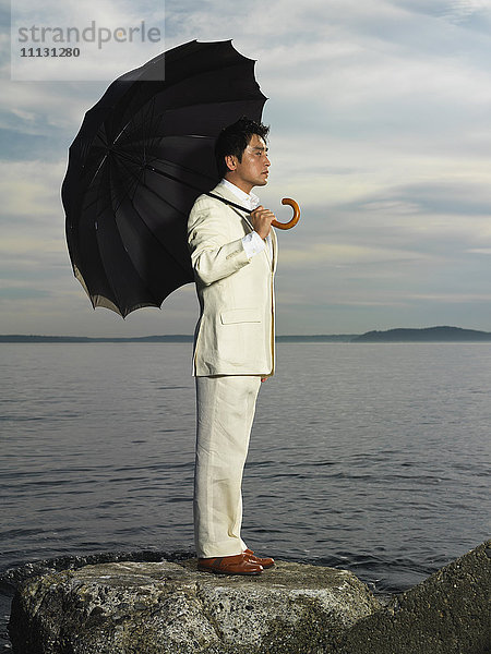 Japanischer Geschäftsmann hält Regenschirm am Meer