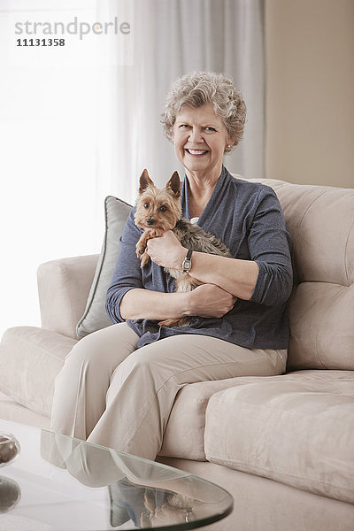 Kaukasische Frau sitzt auf Sofa und hält Hund