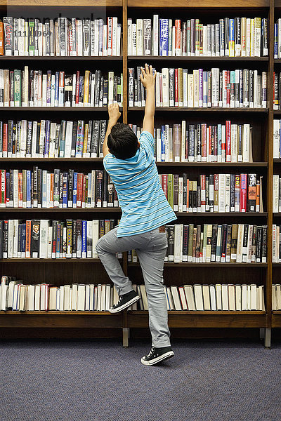 Junge greift nach einem Buch im Bibliotheksregal