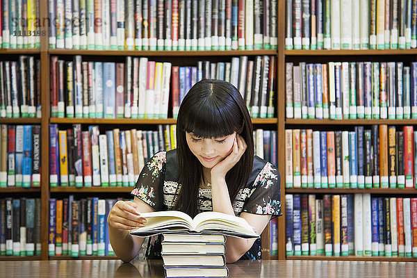 Asiatische Frau  die in einer Bibliothek ein Buch liest
