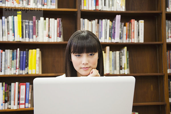 Asiatische Frau benutzt Laptop in einer Bibliothek