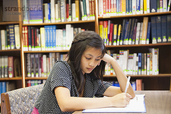 Asiatisches Mädchen macht Hausaufgaben in der Bibliothek