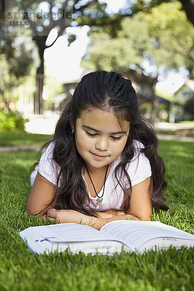 Hispanisches Mädchen liegt im Gras und liest ein Buch