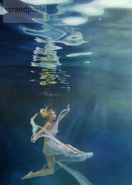 Kaukasische Frau im Kleid schwimmt unter Wasser