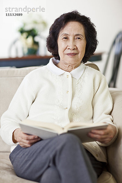 Chinesische Frau auf Sofa beim Lesen eines Buches
