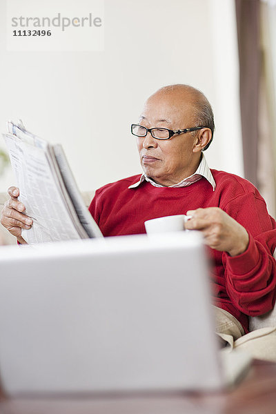 Chinesischer Mann liest Zeitung und trinkt Kaffee