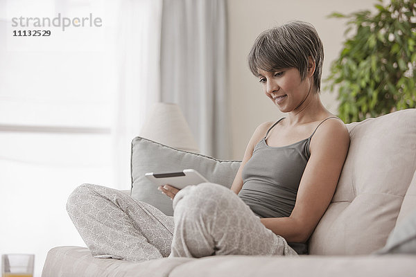 Gemischtrassige Frau auf Sofa mit digitalem Tablet