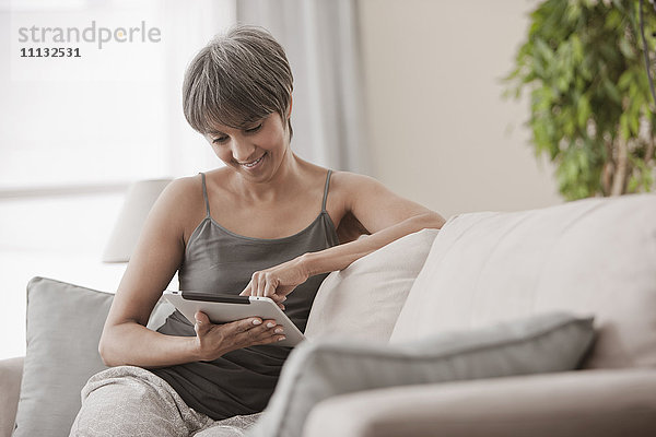 Gemischtrassige Frau auf Sofa mit digitalem Tablet