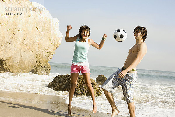 Pärchen spielt mit Fußball am Strand