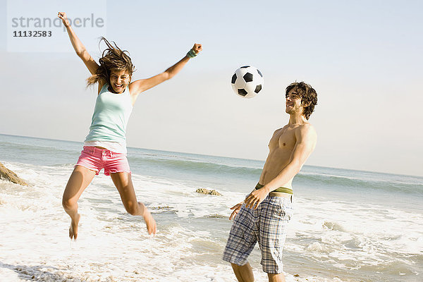 Pärchen spielt mit Fußball am Strand