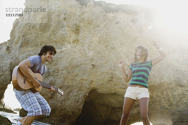 Mann spielt Gitarre für Freundin am Strand