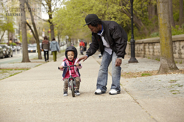 Vater hilft Tochter beim Fahrradfahren auf dem Bürgersteig