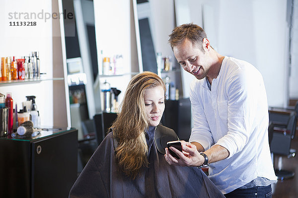 Friseur zeigt einem Kunden sein Handy