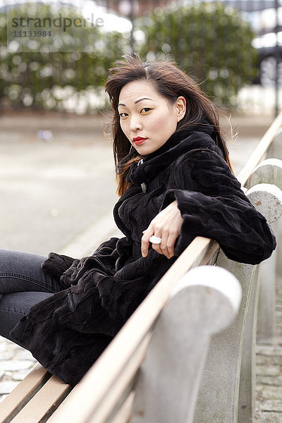Glamouröse koreanische Frau sitzt auf einer Bank