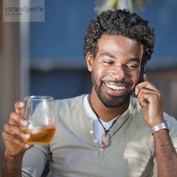 Schwarzer Mann  der mit einem Handy telefoniert und trinkt