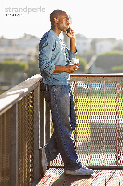 Schwarzer Mann spricht mit Handy auf Balkon