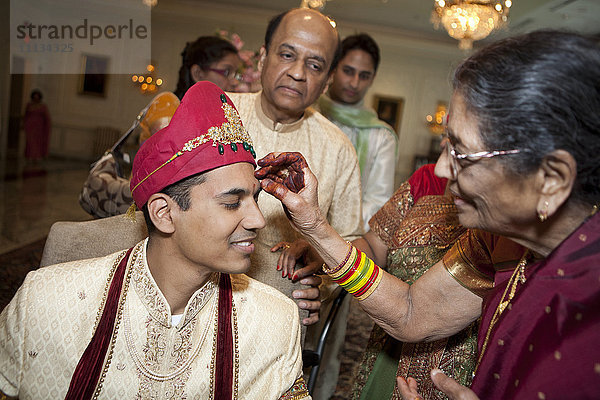 Indische Frau markiert das Gesicht des Bräutigams