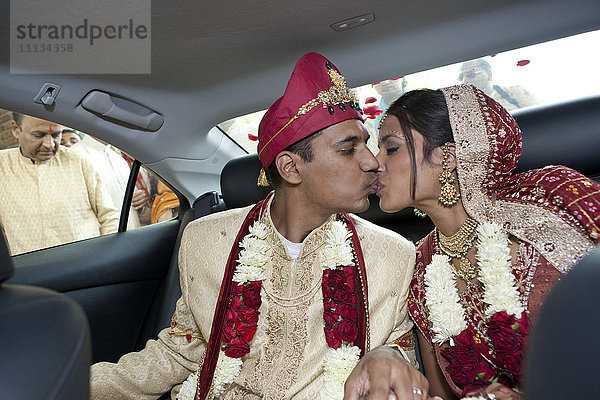 Indische Braut und Bräutigam in traditioneller Kleidung  die sich im Auto küssen