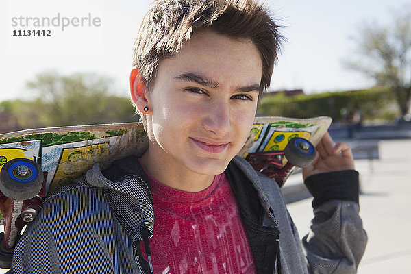 Lächelnder Junge gemischter Rasse hält Skateboard