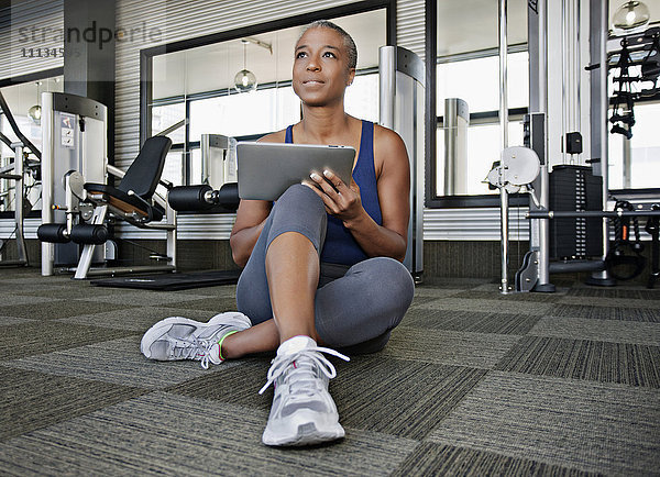 Afroamerikanische Frau benutzt digitales Tablet im Fitnessstudio