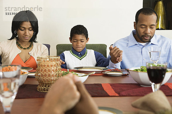 Afroamerikanische Familie spricht am Esstisch das Tischgebet